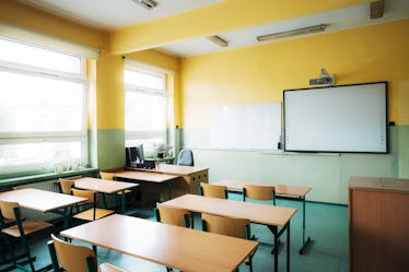 Rear view of an empty classroom in elementary school. Wooden chairs and desks inside the classroom w...