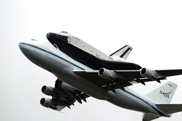 The NASA space shuttle Enterprise, riding on top of a modified jumbo jet, flying at low altitude pas...