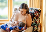 A mother breastfeeding her newborn child. She is sitting on a comfortable chair in a living room at ...