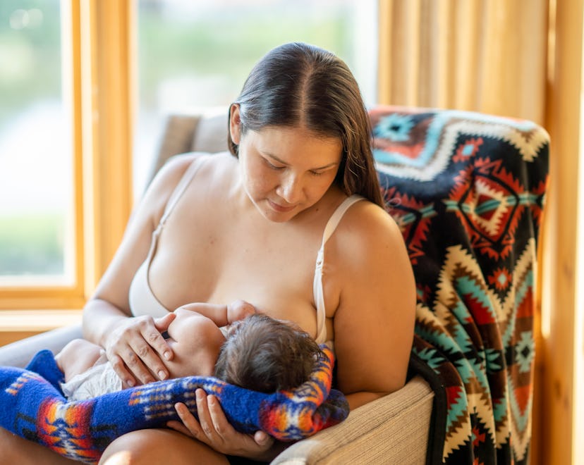 A mother breastfeeding her newborn child. She is sitting on a comfortable chair in a living room at ...
