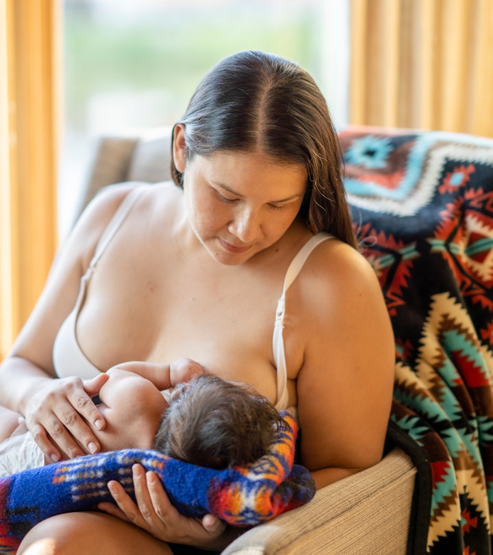 A mother breastfeeding her newborn child. She is sitting on a comfortable chair in a living room at ...