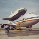 Space Shuttle Enterprise (OV-101) arrives atop NASA 905, a 747 carrier aircraft in the background, a...