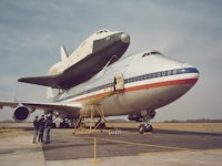 Space Shuttle Enterprise (OV-101) arrives atop NASA 905, a 747 carrier aircraft in the background, a...