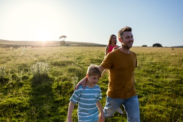 A dad walks with his son in a grass field, his wife in the background.