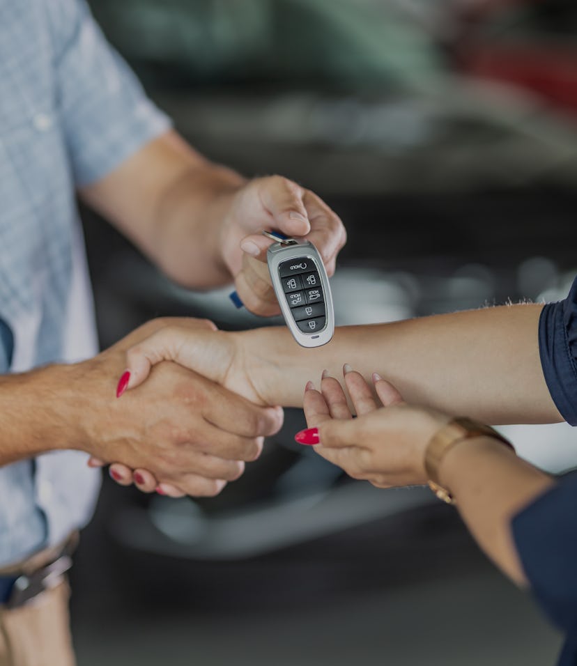 Dealer giving key to new owner and shaking hands in auto show or salon.