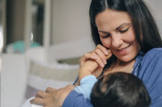 Young beautiful mother breastfeeding her newborn baby boy, while father working on laptop