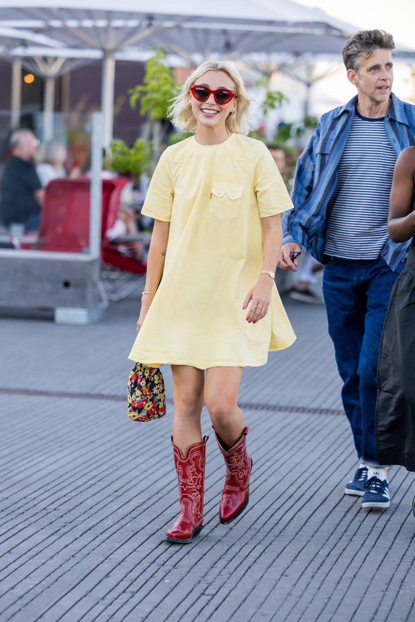 Emma Chamberlain wearing a yellow dress, red glasses and cowboy boots with a colorful bag at Copenha...