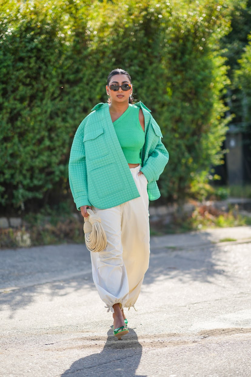 COPENHAGEN, DENMARK - AUGUST 09: A guest wears brown sunglasses, gold earrings, a green ribbed / asy...