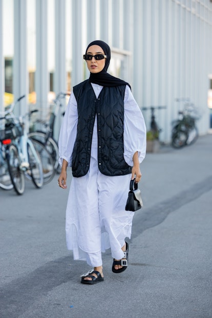 COPENHAGEN, DENMARK - AUGUST 11: A guest is seen wearing black vest, white dress, black bag outside ...