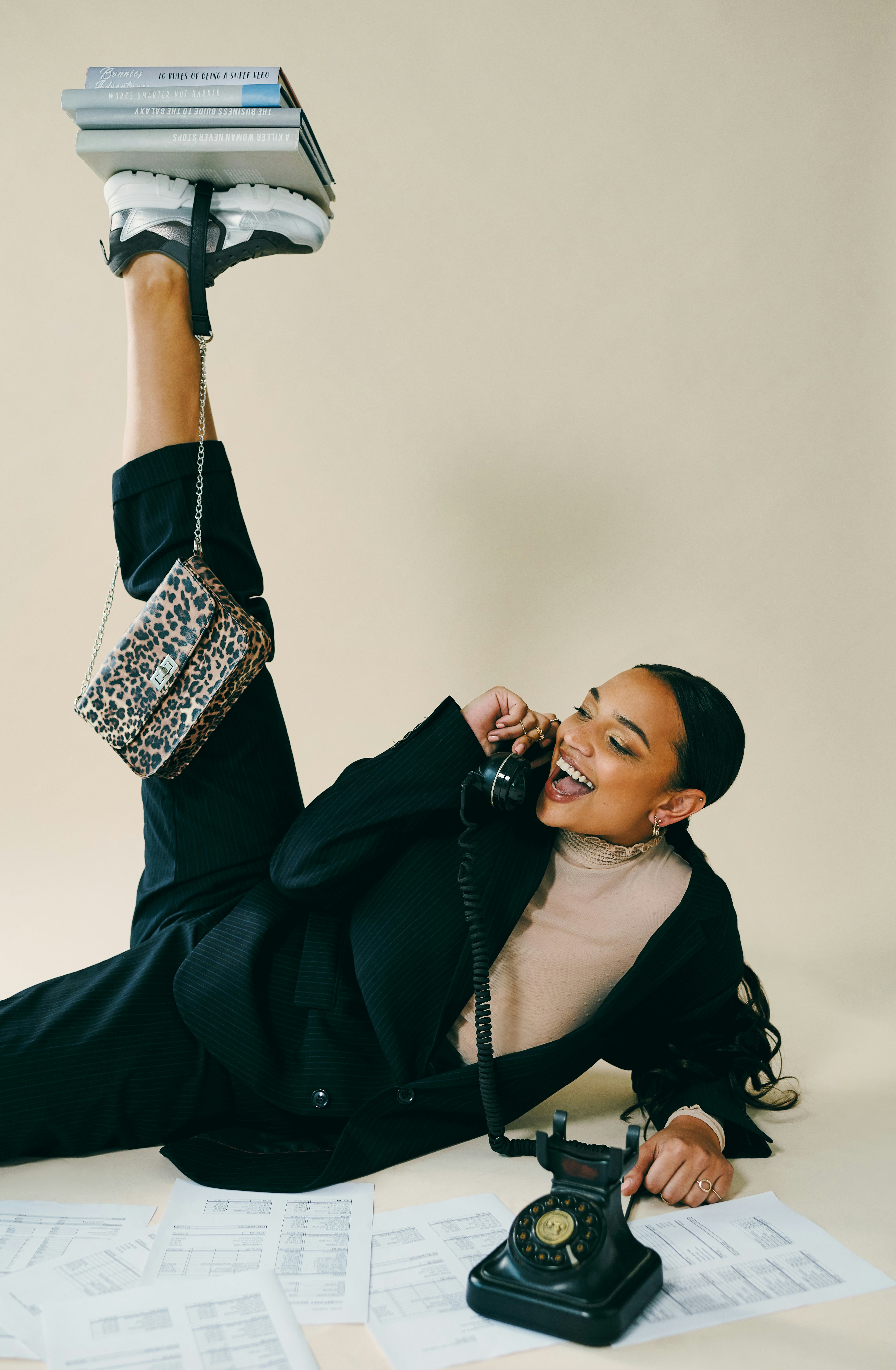Young woman balancing a pile of books on her foot while talking on the phone during the 2022 new moo...