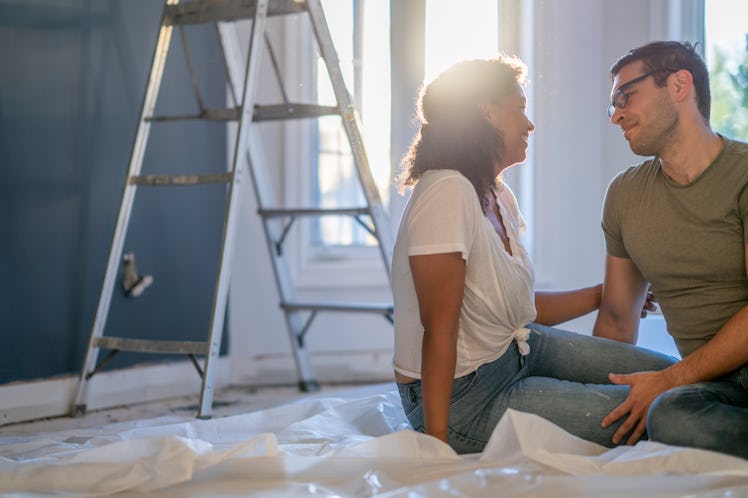 A young couple sit closely together on the floor of their new home as they take a break from renovat...
