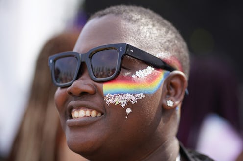 A woman with a buzz cut and black sunglasses, with a rainbow (LGBTQ) flag painted on her cheek