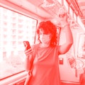 A young woman with curly hair riding the light rail wearing a face mask and checking her smartphone.