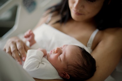 Newborn girl sleeps in her mom arms in an article about if your newborn baby is lethargic baby or ju...