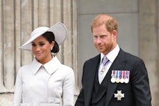 Meghan and Harry walk out of a building; Meghan wears an all white ensemble and Harry is in a milita...