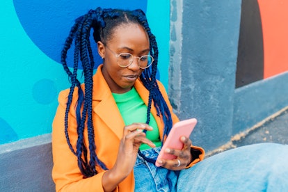 Woman with braids sitting by colorful wall, researching astrology elements