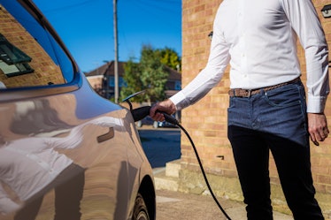 Color image depicting a man charging his electric vehicle at home.