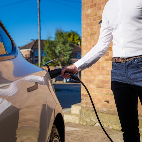 Color image depicting a man charging his electric vehicle at home.