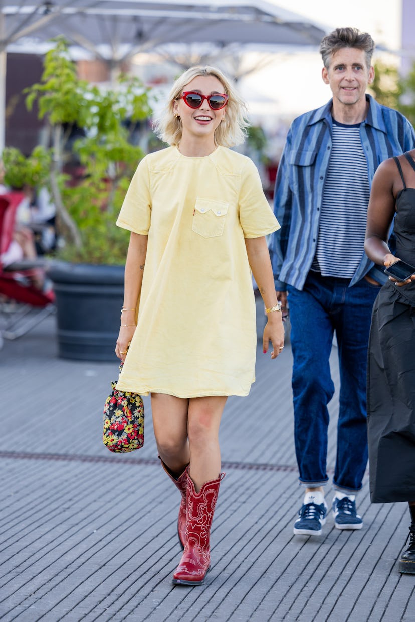 Emma Chamberlain seen wearing yellow dress, red cowboy boots, bag with floral print outside Ganni du...