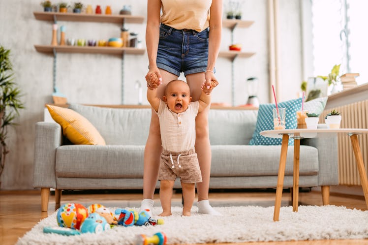 Young mother teaching her baby boy how to walk in an apartment.