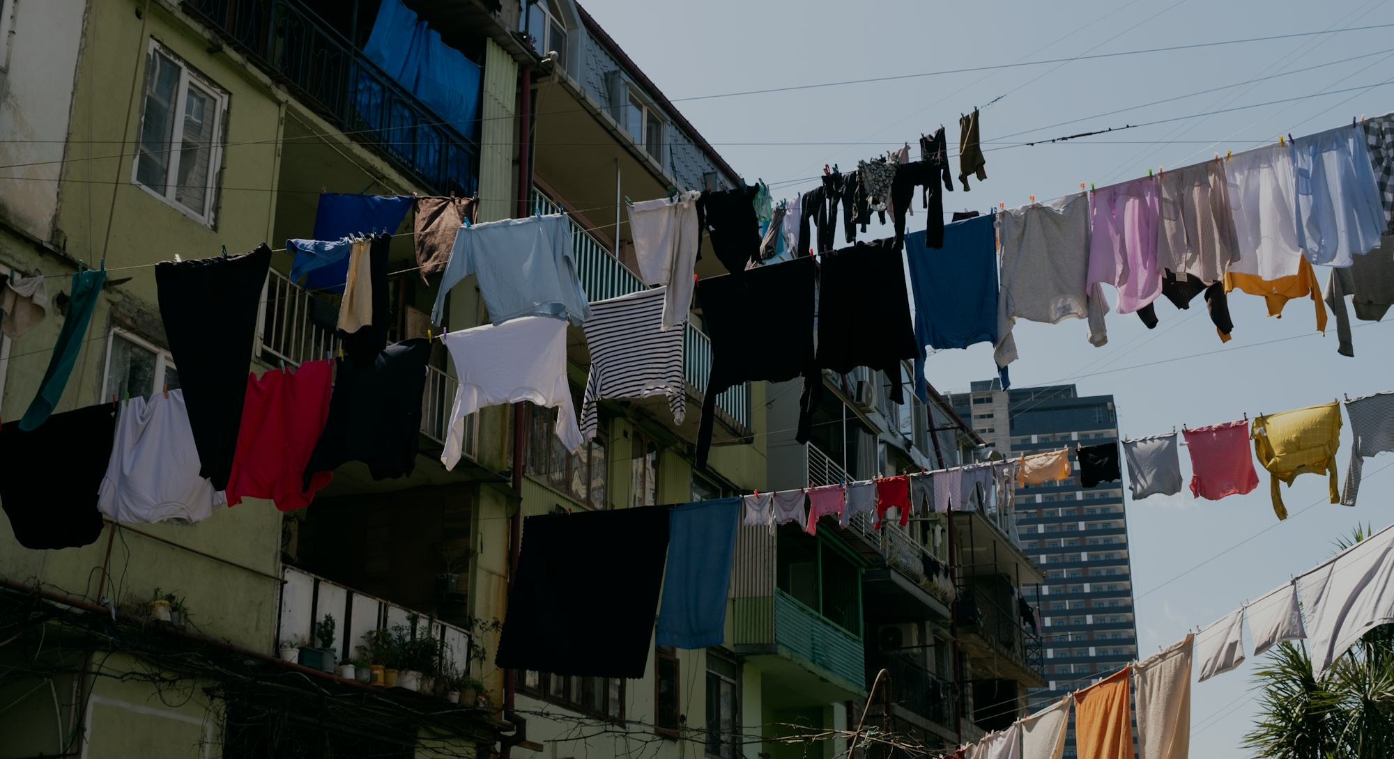 Clean sweaters, trousers and T-shirts hang on a rope outside on a sunny summer day, against a blue s...