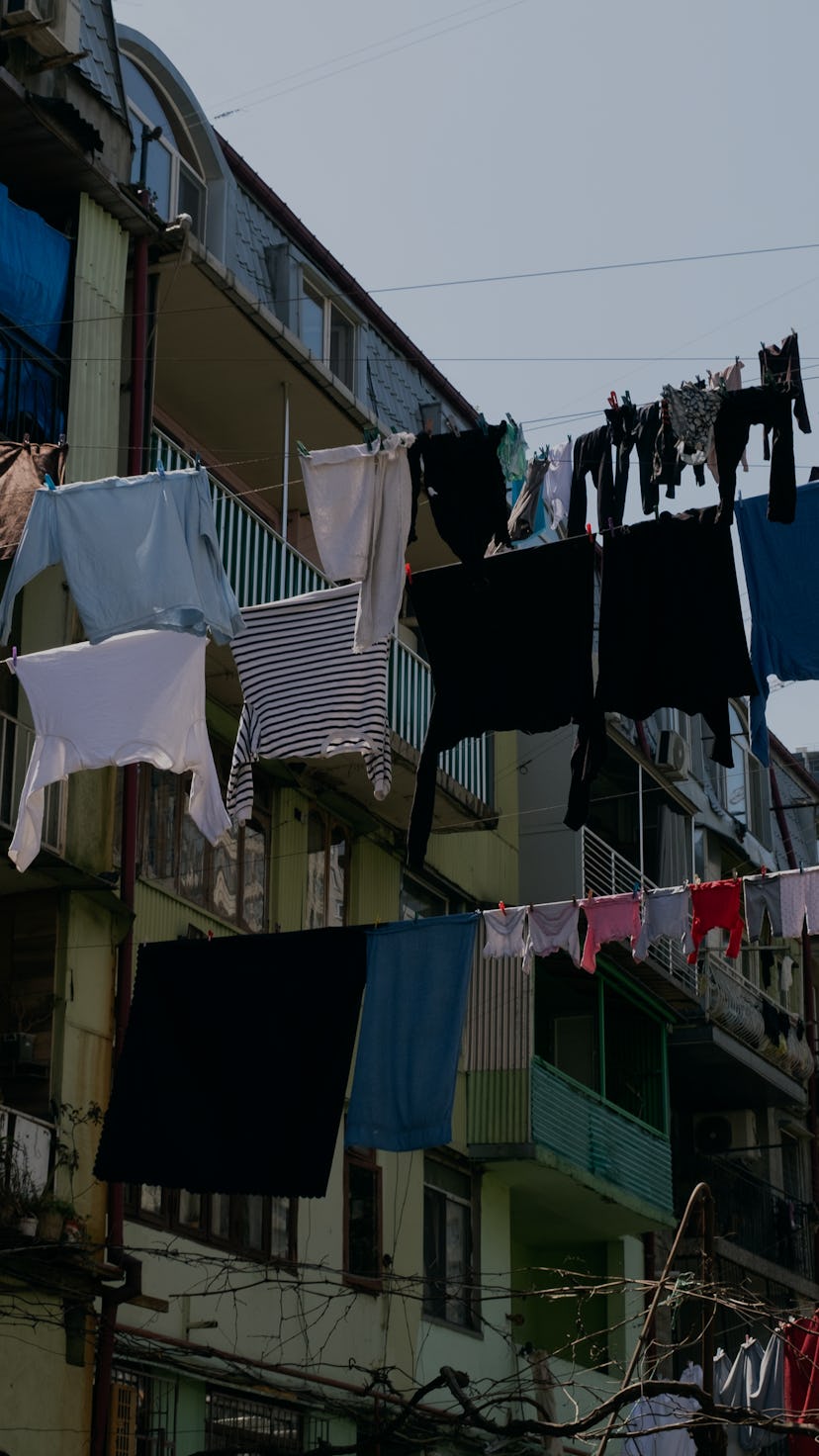 Clean sweaters, trousers and T-shirts hang on a rope outside on a sunny summer day, against a blue s...