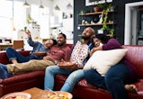 Four friends enjoying TV dinner with takeaway curry, sitting on sofa and relaxing