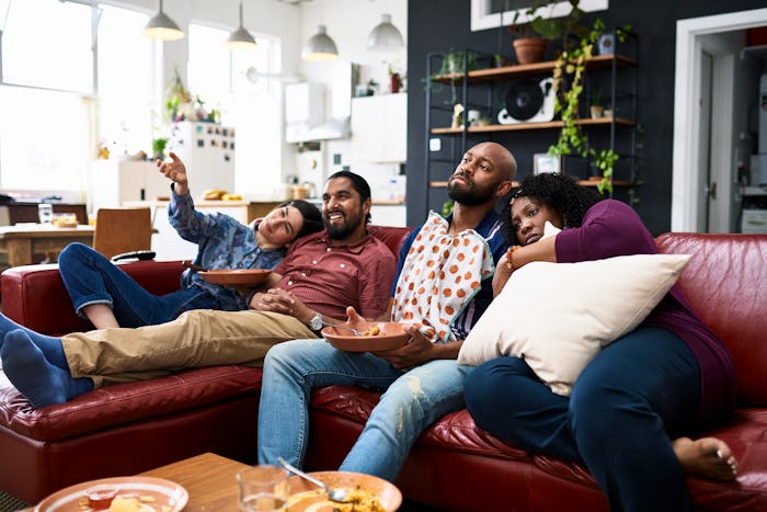 Four friends enjoying TV dinner with takeaway curry, sitting on sofa and relaxing