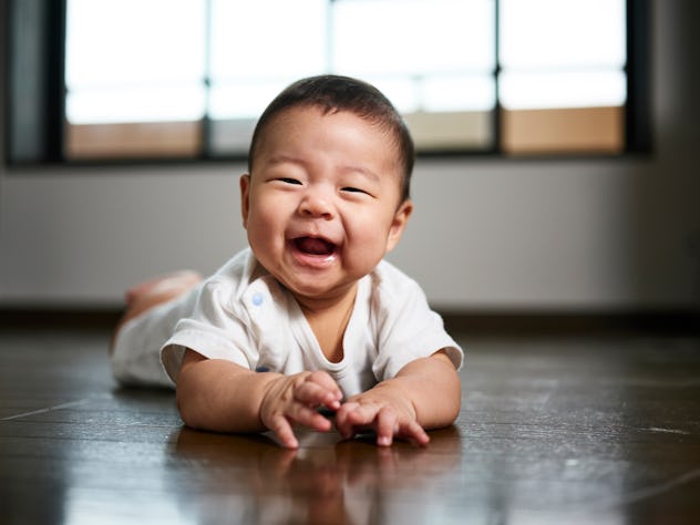 A six month old baby boy smiling and crawling on the floor in an article about baby names that start...