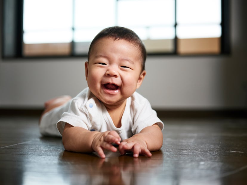 A six month old baby boy smiling and crawling on the floor in an article about baby names that start...