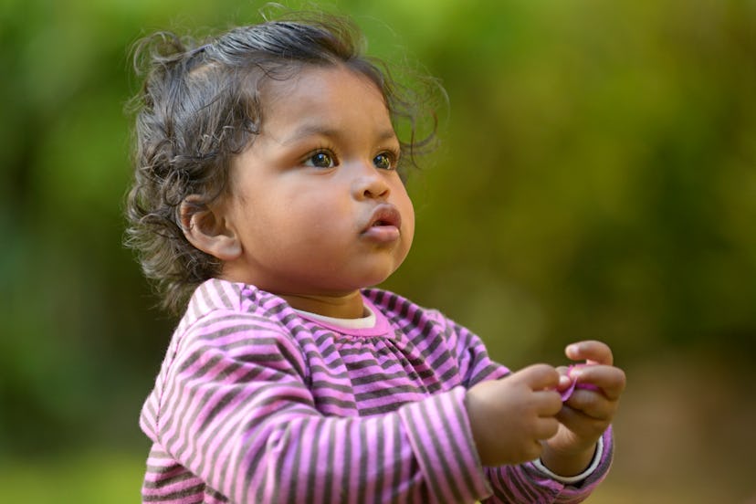 a baby girl in a purple striped dress looking out while paying in a garden in an article about the b...