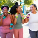 A multiracial group of three women exercising together in a city park. They are power walking with h...