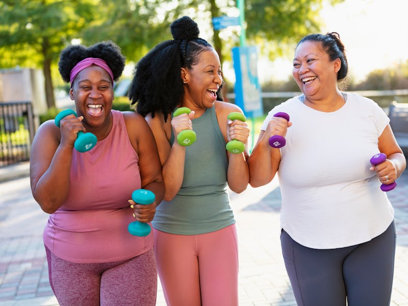 A multiracial group of three women exercising together in a city park. They are power walking with h...