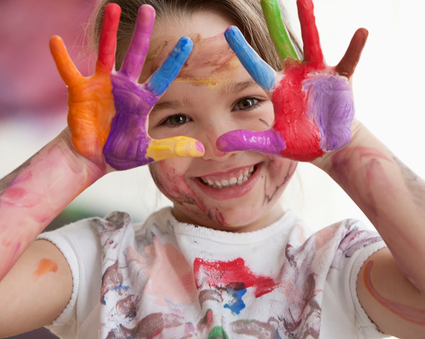 A little girl holding both hands with paint on them in the air, smiling