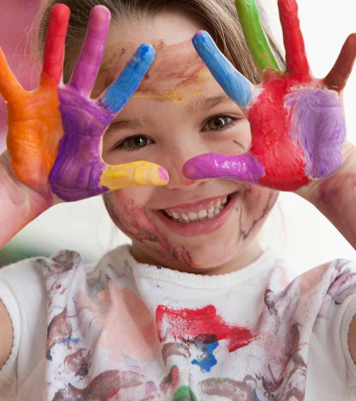A little girl holding both hands with paint on them in the air, smiling