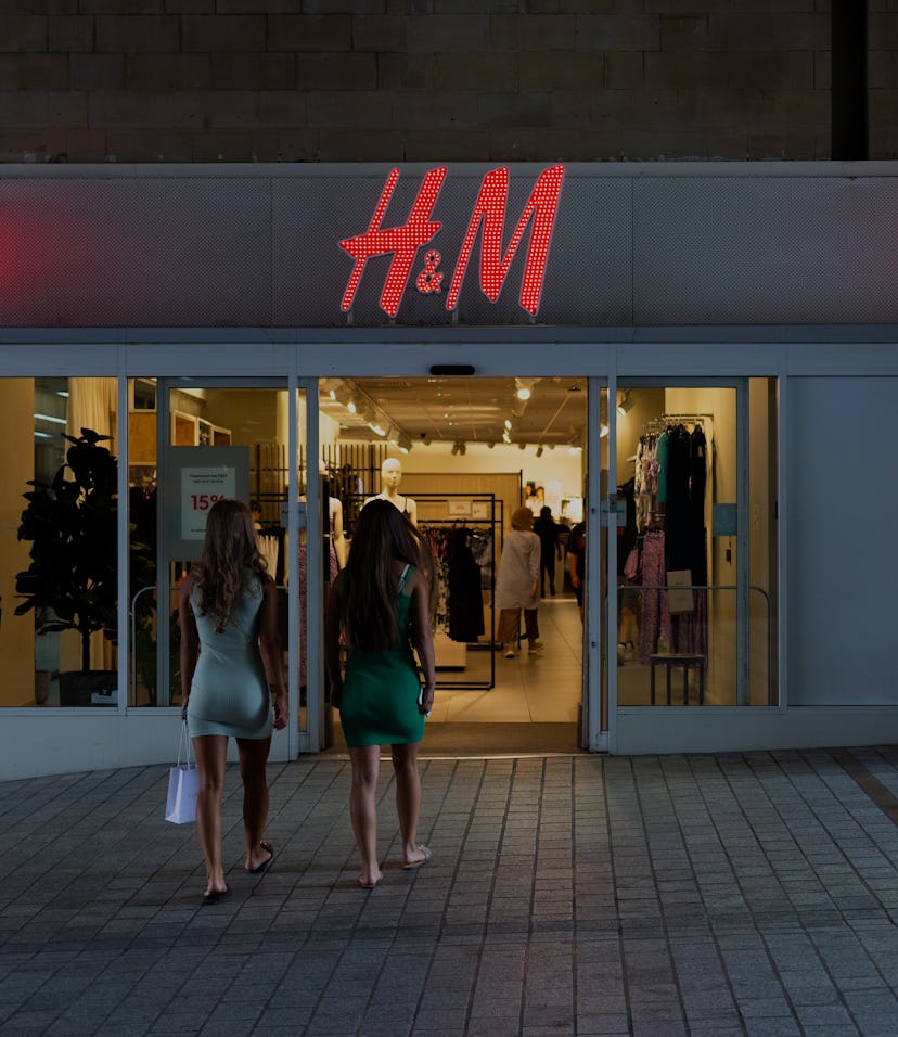 Two young women, one carrying a small shopping bag, approach the entrance to a high street branch of...