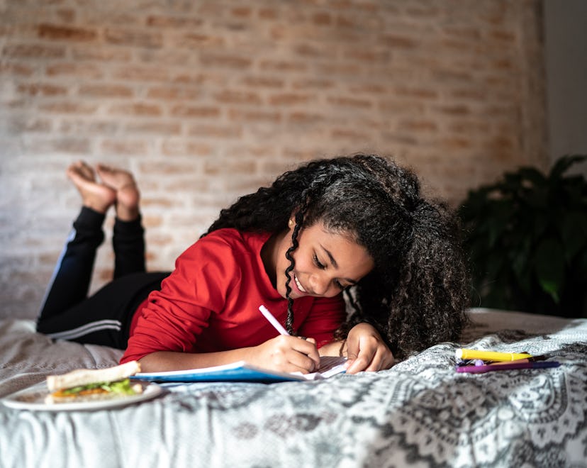 Girl writing on note pad or dairy lying on bed at home, kid writing in cute notebook for back to sch...