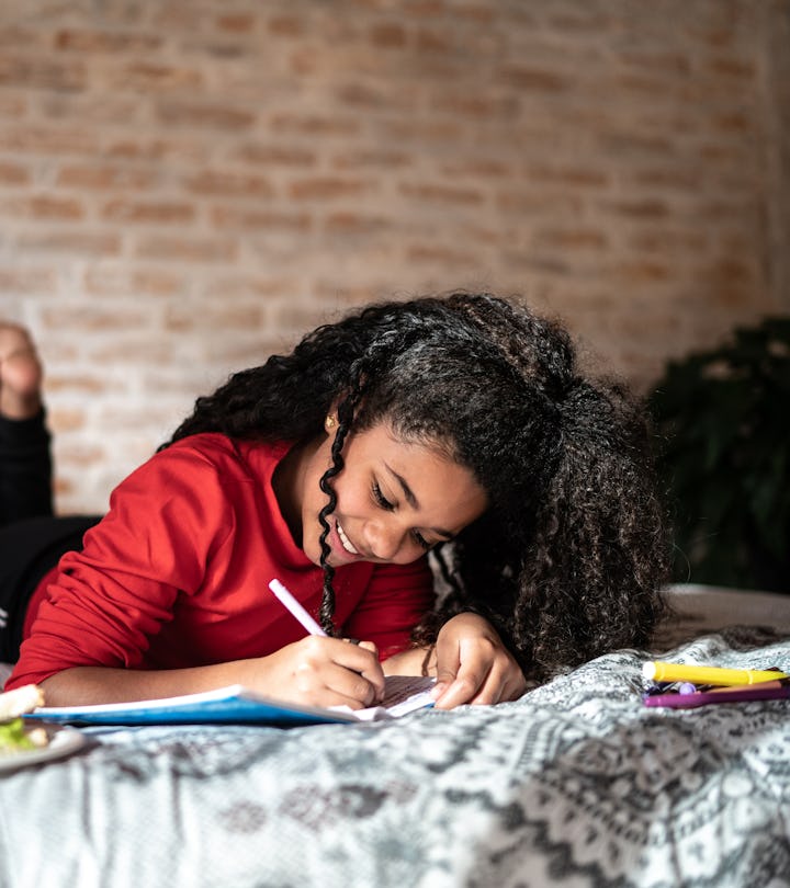 Girl writing on note pad or dairy lying on bed at home, kid writing in cute notebook for back to sch...