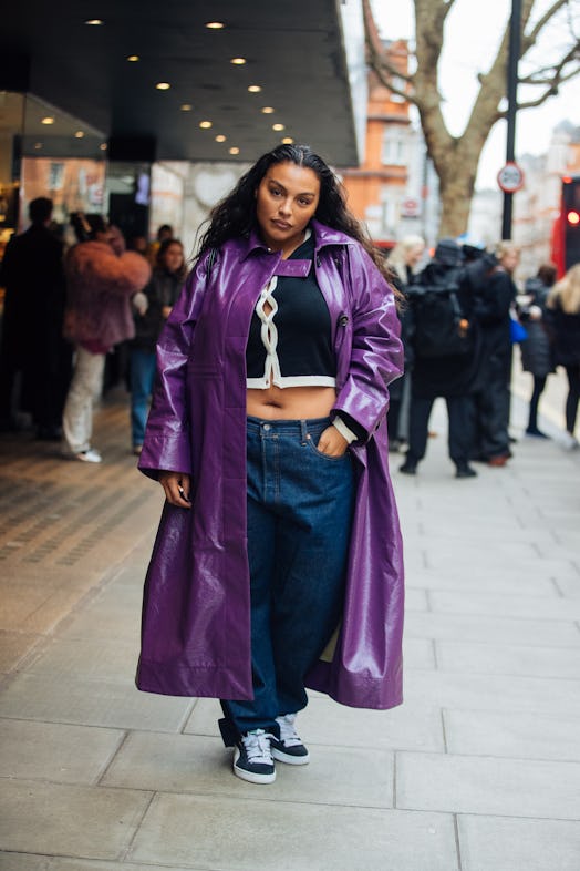 Paloma Elsesser wears a purple leather trench coat, black cropped cardigan, blue jeans, and black Pu...