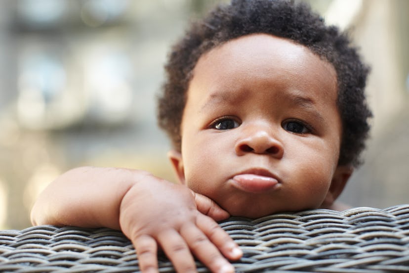 Little toddler boy standing and resting his head on a chair 