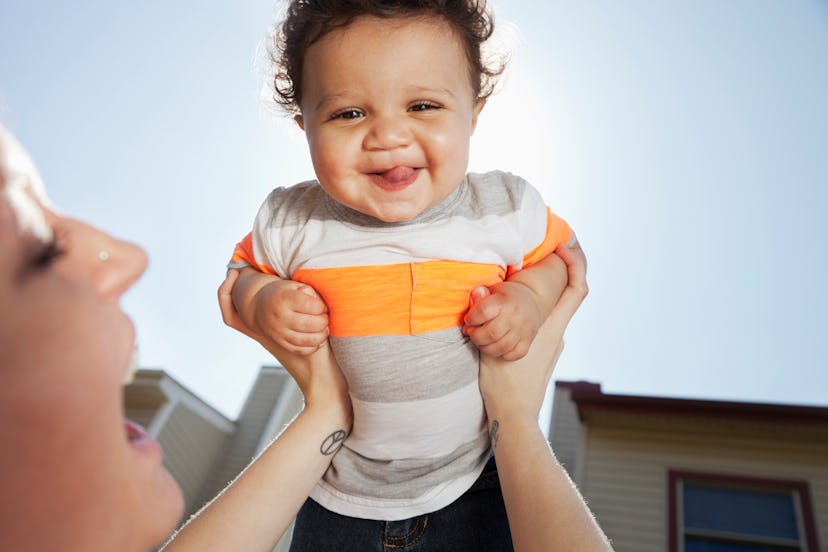 Baby boy smiling while his mother is holding him in the sunshine 