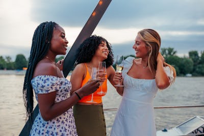 Three friends drinking wine on a boat as they discuss the ideal solo destination trip for their sign