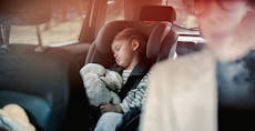 Cute girl napping with her toy in child safety seat while her unrecognizable mother driving car.