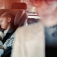 Cute girl napping with her toy in child safety seat while her unrecognizable mother driving car.