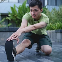 A man stretching his body with his hand reaching to toes while kneeling down