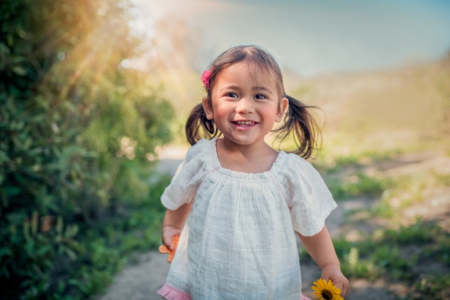 A 2 year old girl smiles as she plays outdoors with a yellow daisy. Disney baby names & Disney girl ...
