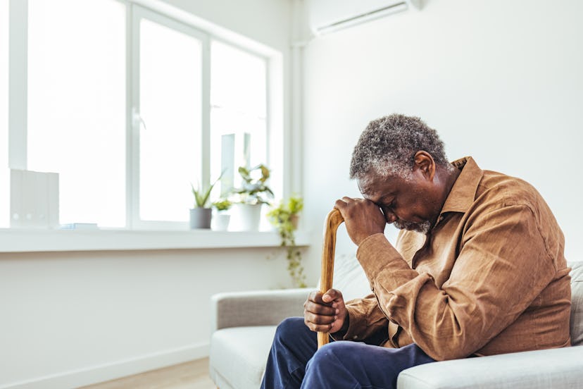 Thoughtful elderly man sitting alone at home with his walking cane