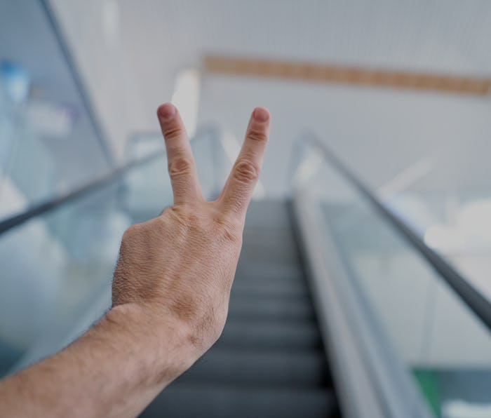 a person climbing an escalator while holding up two fingers in a building