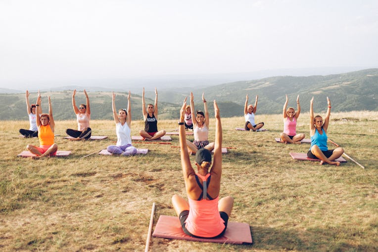 Group of women doing yoga exercises on a hill , in non-urban area under open and clear skies in fron...