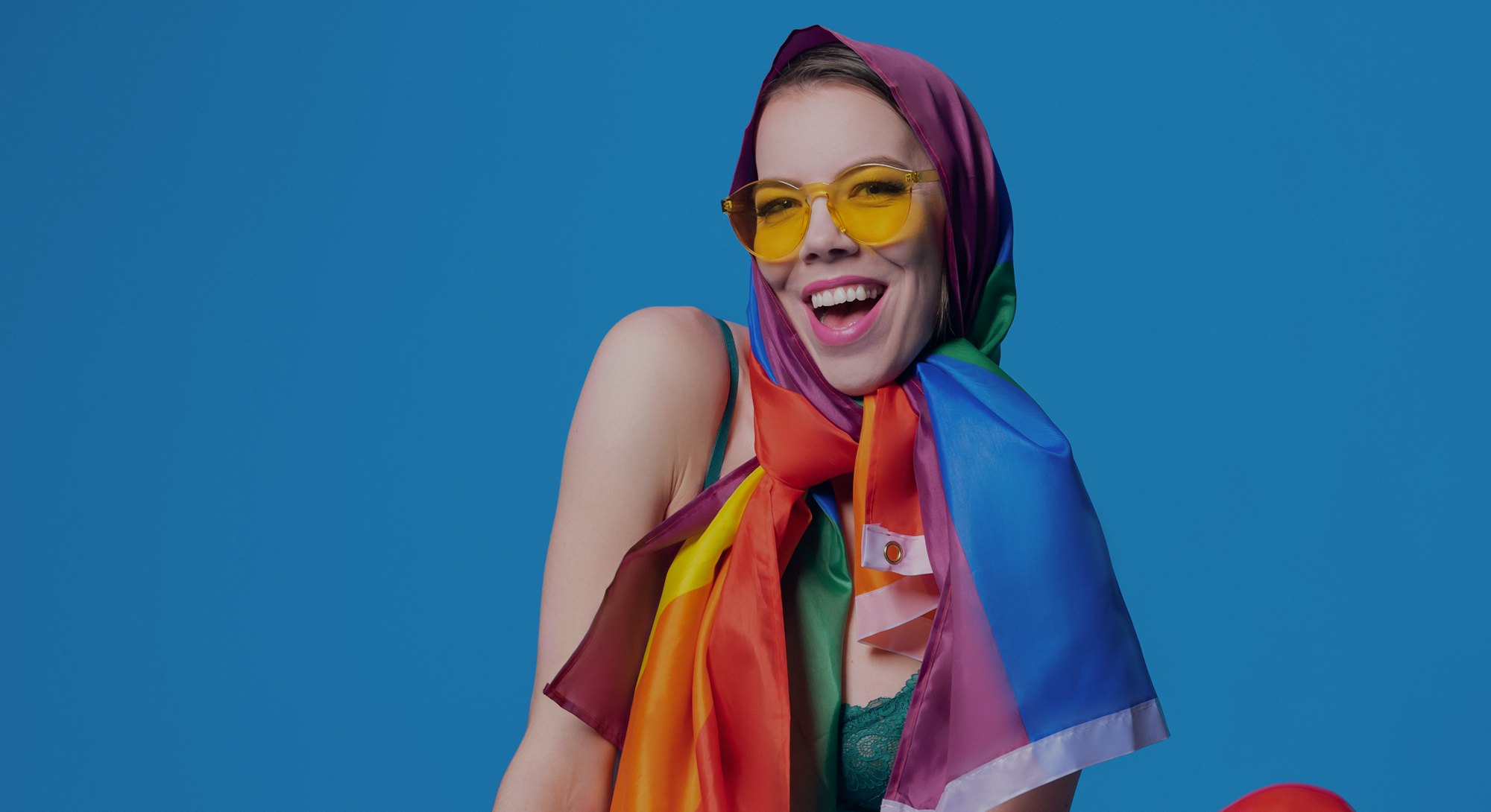 Cheerful fit homosexual woman in bra holding colorful rainbow LGBT flag against blue background in l...